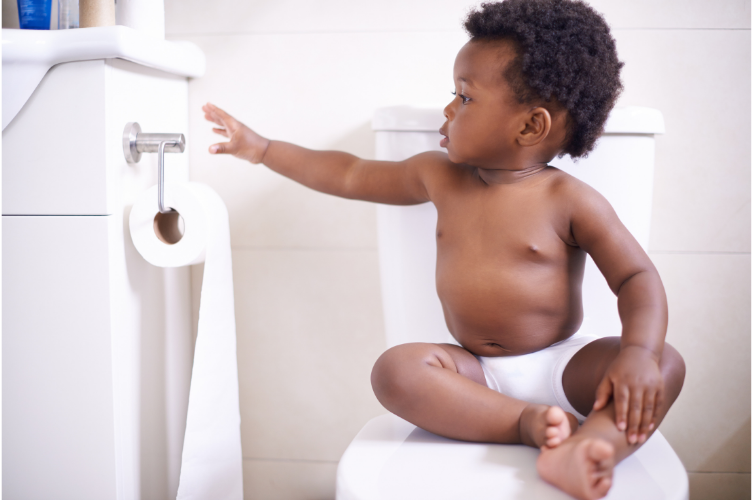 Toddler potty training on toilet reaching for toilet paper in modern bathroom setting.
